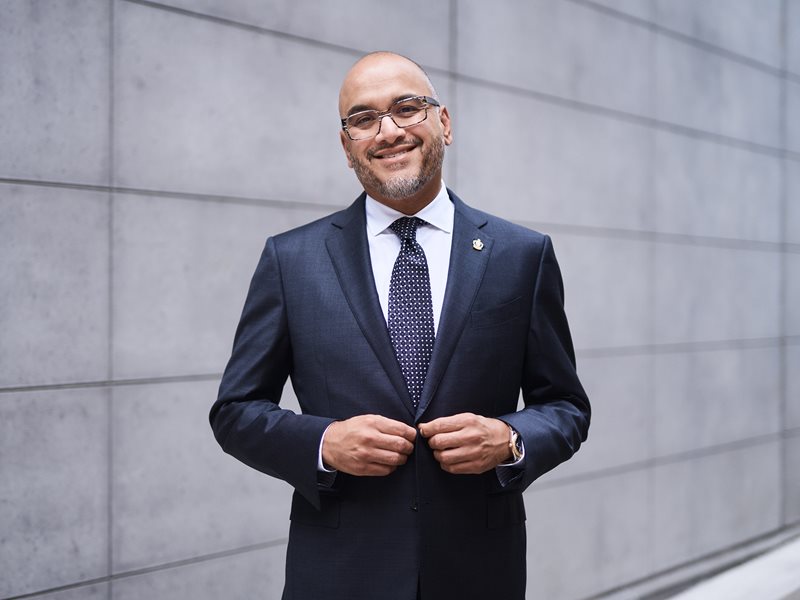 Dr. Ian Preyra smiling standing outside in front of a grey slate wall.